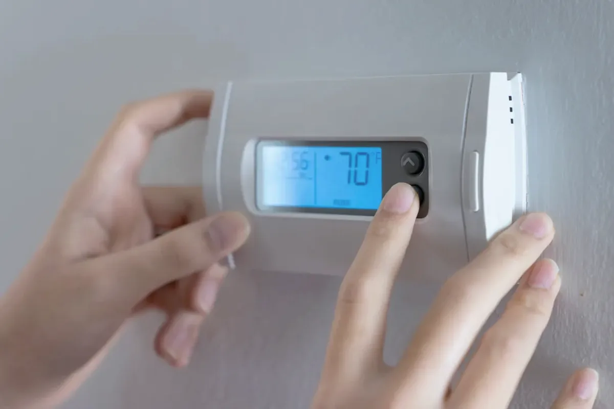 Hands adjusting a digital wall thermostat