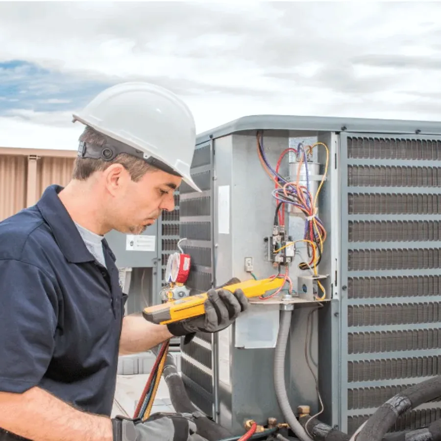 HVAC technician in a hard hat testing an outdoor air conditioner with a multimeter